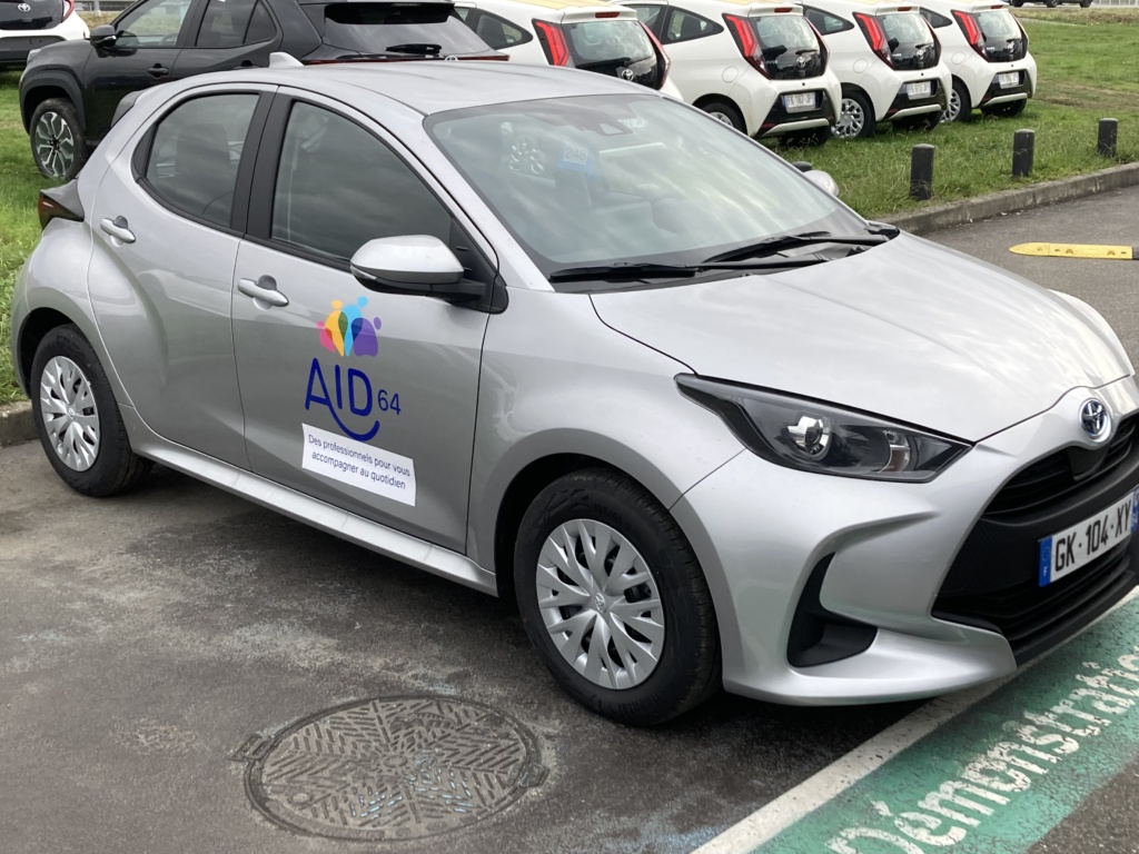 Voiture grise avec logo AID 64 garée.